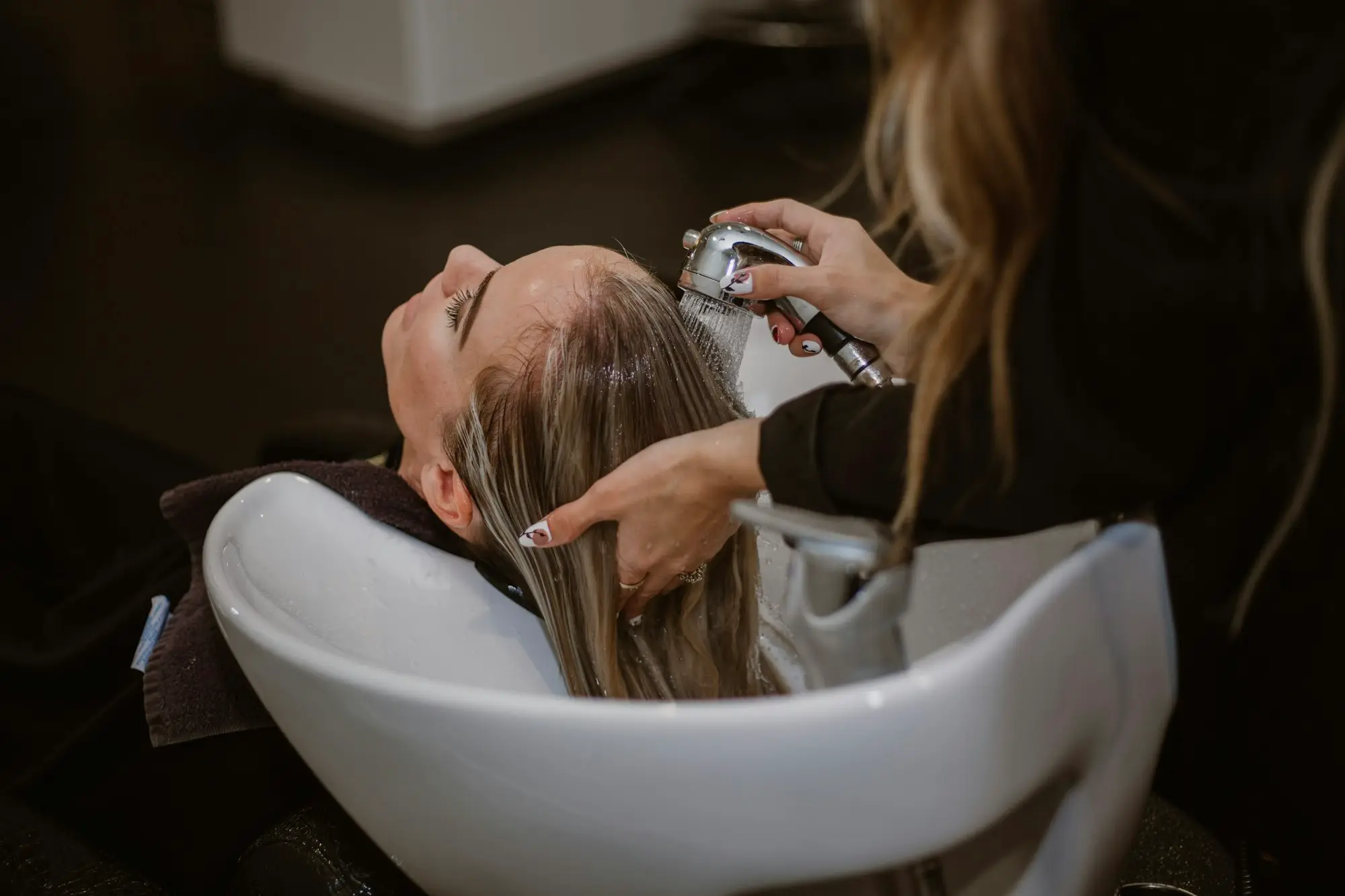 Hair stylist washing a client's hair at a salon basin